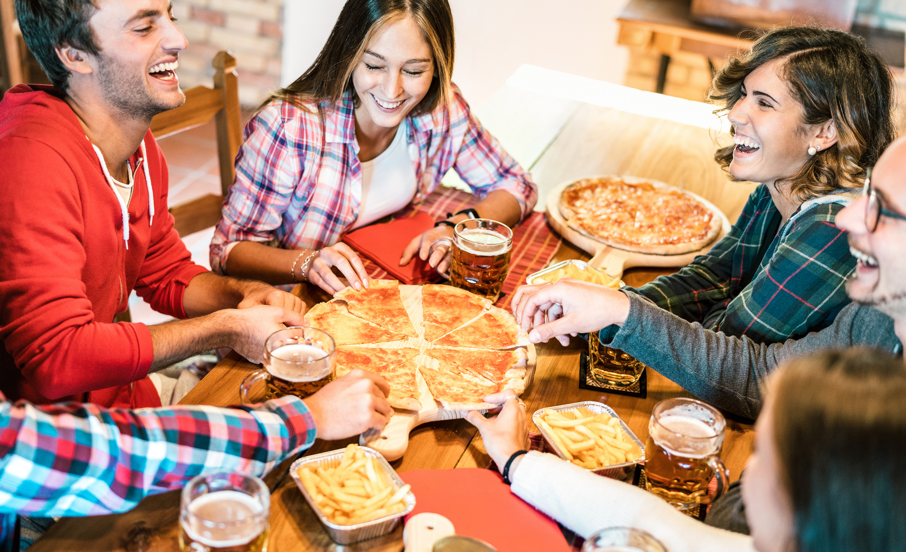 Young friends on genuine laugh while eating pizza at home on family reunion - Friendship concept with happy people enjoying time together having fun at pizzeria drinking brew pints - Warm vivid filter
